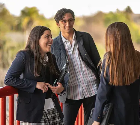 Tres estudiantes conversando al aire libre en el campus de la escuela durante el recreo
